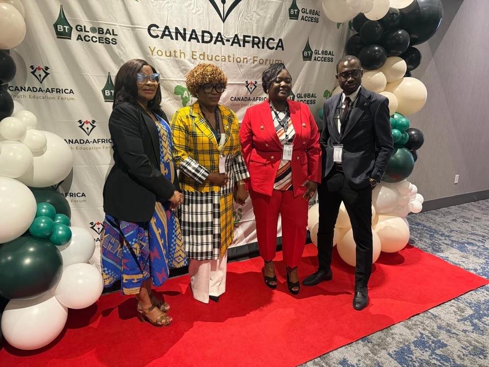 Four delegates stand together on a red carpet in front of a Canada-Africa Youth Education Forum backdrop, framed by green, black and white balloons.