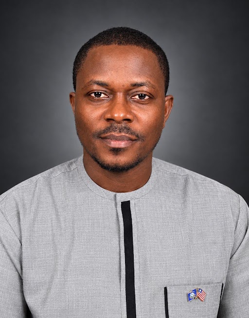 Lansana M. Kromah, in a grey collarless shirt, against a plain dark background.